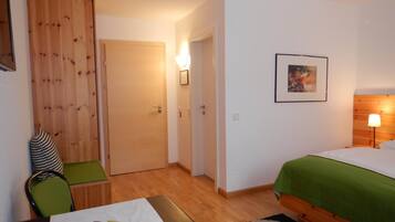 Una habitación de hotel con una cama, un escritorio con silla, un armario de madera, una puerta y una lámpara de pared.