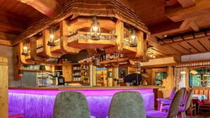 A bar area with wooden beams, bar stools, and a neon-lit counter. - Ländenhof (Mayrhofen)