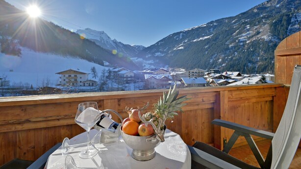 A wooden deck with a table set for a meal, overlooking a snowy mountain landscape with a clear sky. - Ländenhof (Mayrhofen)