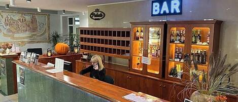 A bar area with a reception desk, a sign indicating the bar, and shelves with bottles.