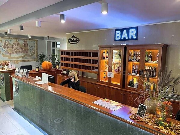 A bar area with a reception desk, a sign indicating the bar, and shelves with bottles.