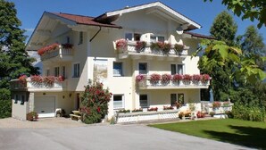 A multi-story building with balconies adorned with flowers, a covered driveway, and a well-maintained lawn. - Haus Alpina (Schladming)