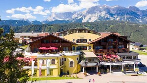 Un hotel con fachada amarilla, varios balcones y vista a las montañas al fondo.