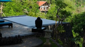 Un área de piscina con sillones de descanso, un muro de piedra y vistas a una casa rodeada de vegetación.