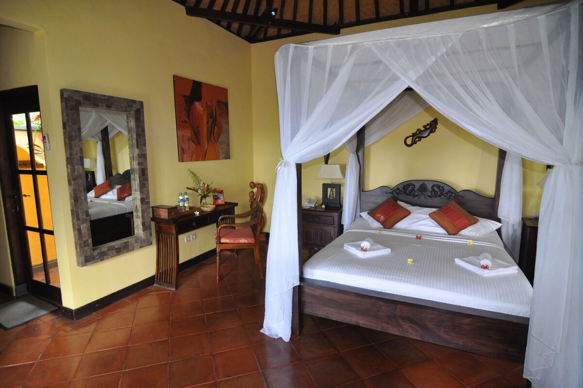 A room with a bed under a canopy, a desk with a chair, a mirror, and a painting on the wall.