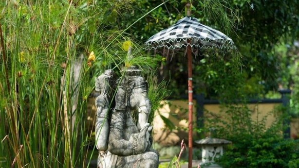 Una estatua de jardín con un paraguas, rodeada de follaje.