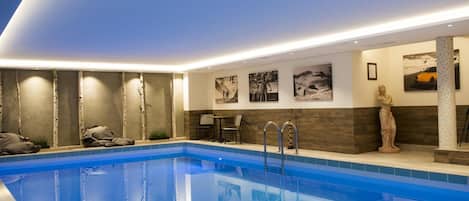 A modern indoor swimming pool with clear blue water, surrounded by walls with framed pictures and a statue.
