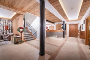 A spacious living area with a staircase, wooden flooring, and a kitchen area with wooden cabinets. - Hotel Garni Entstrasser (Kitzbühel)
