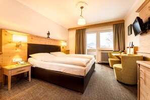 A hotel room with a bed, bedside table, lamp, chair, and a television. - Hotel Garni Entstrasser (Kitzbühel)