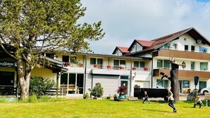 A two-story building with a balcony, a garage, and a tree in the foreground. - Tanneneck (Löffingen)