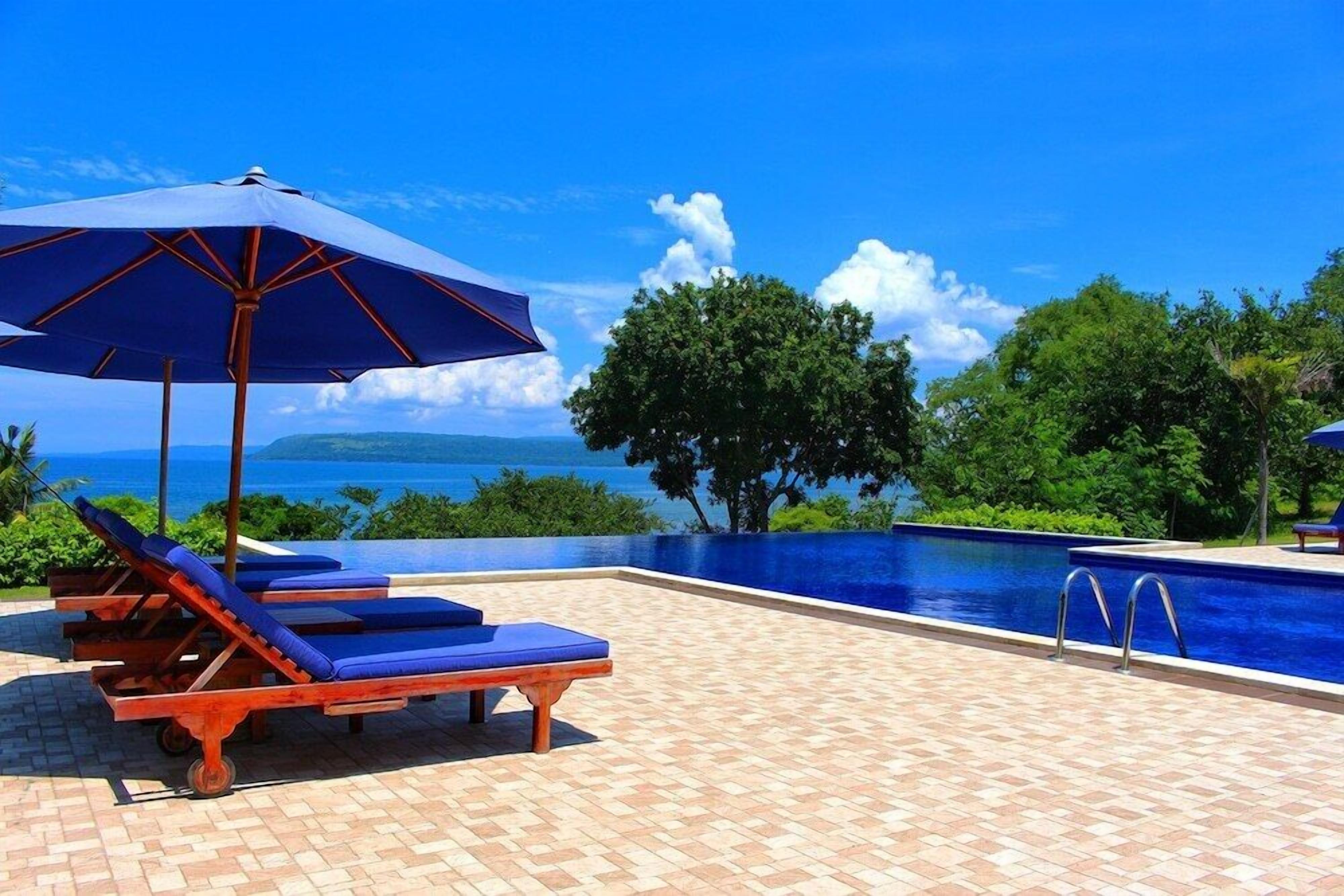Un espace aménagé au bord de la piscine, avec des chaises longues et un parasol, offrant une vue dégagée sur une piscine aux eaux cristallines et sur l’océan.