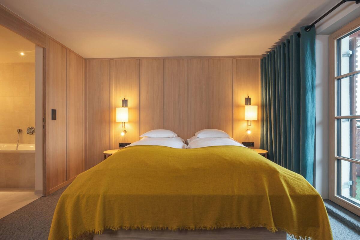 Une chambre d’hôtel avec un lit, deux lampes de chevet, une fenêtre avec des rideaux et un mur en bois.