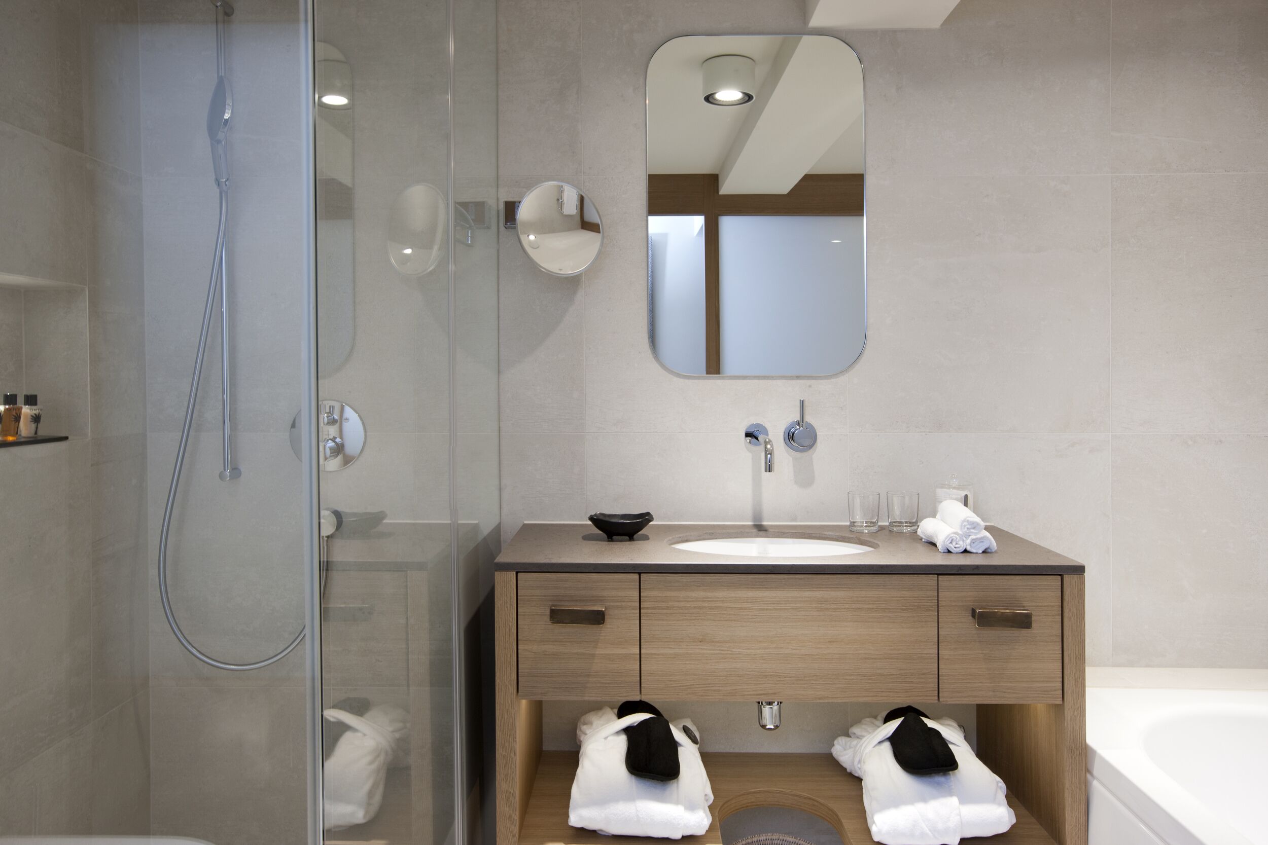 A modern bathroom with a glass-enclosed shower, a wooden vanity with a sink, and a large mirror.