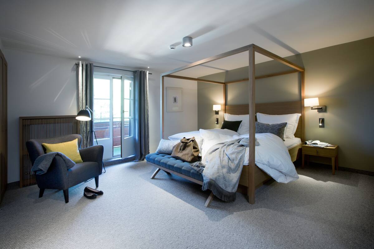 Un lit à baldaquin avec une structure en bois, un canapé avec un coussin jaune, une chaise et une table de chevet avec une lampe.