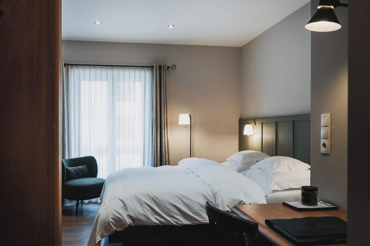 Une chambre d’hôtel avec deux lits, un bureau, une chaise et une lampe.