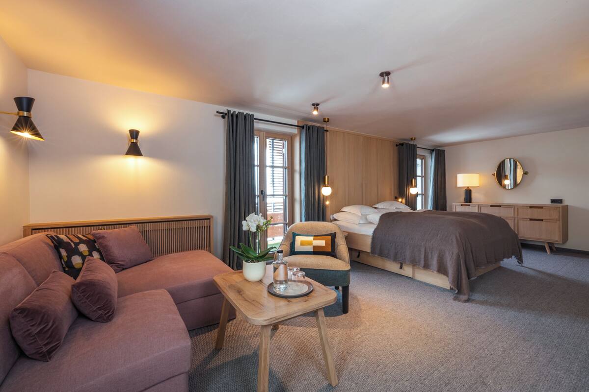 Une chambre d’hôtel avec un lit, un canapé, une table avec un vase et un verre, et une lampe de chevet.