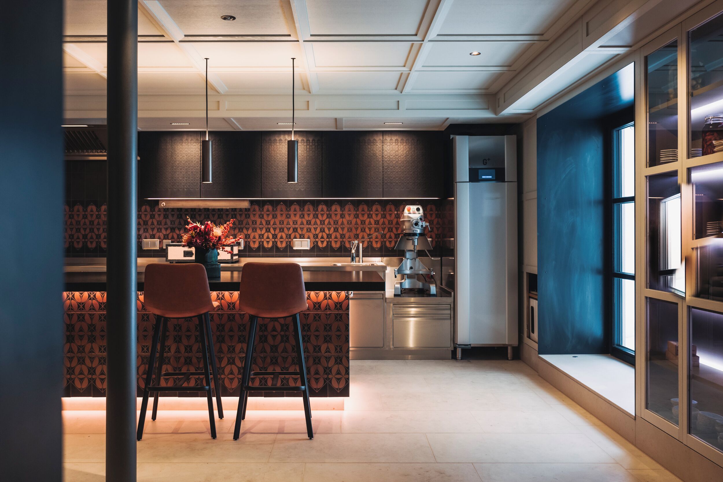 A modern kitchen with dark patterned backsplash, stainless steel appliances, and pendant lighting.
