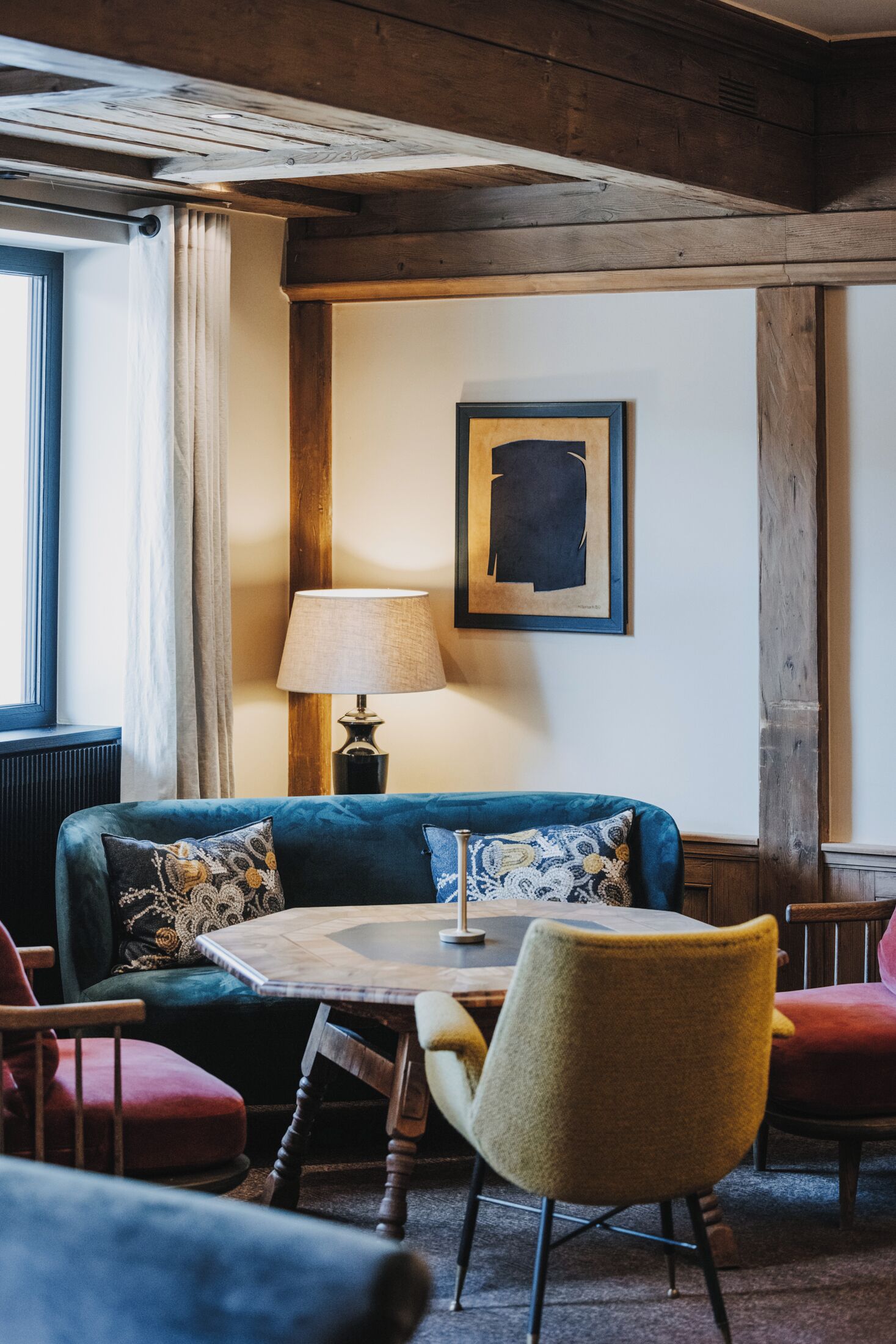 Una habitación acogedora con un sofá azul, una mesa de madera y una silla amarilla. Hay una lámpara sobre la mesa y un cuadro en la pared.