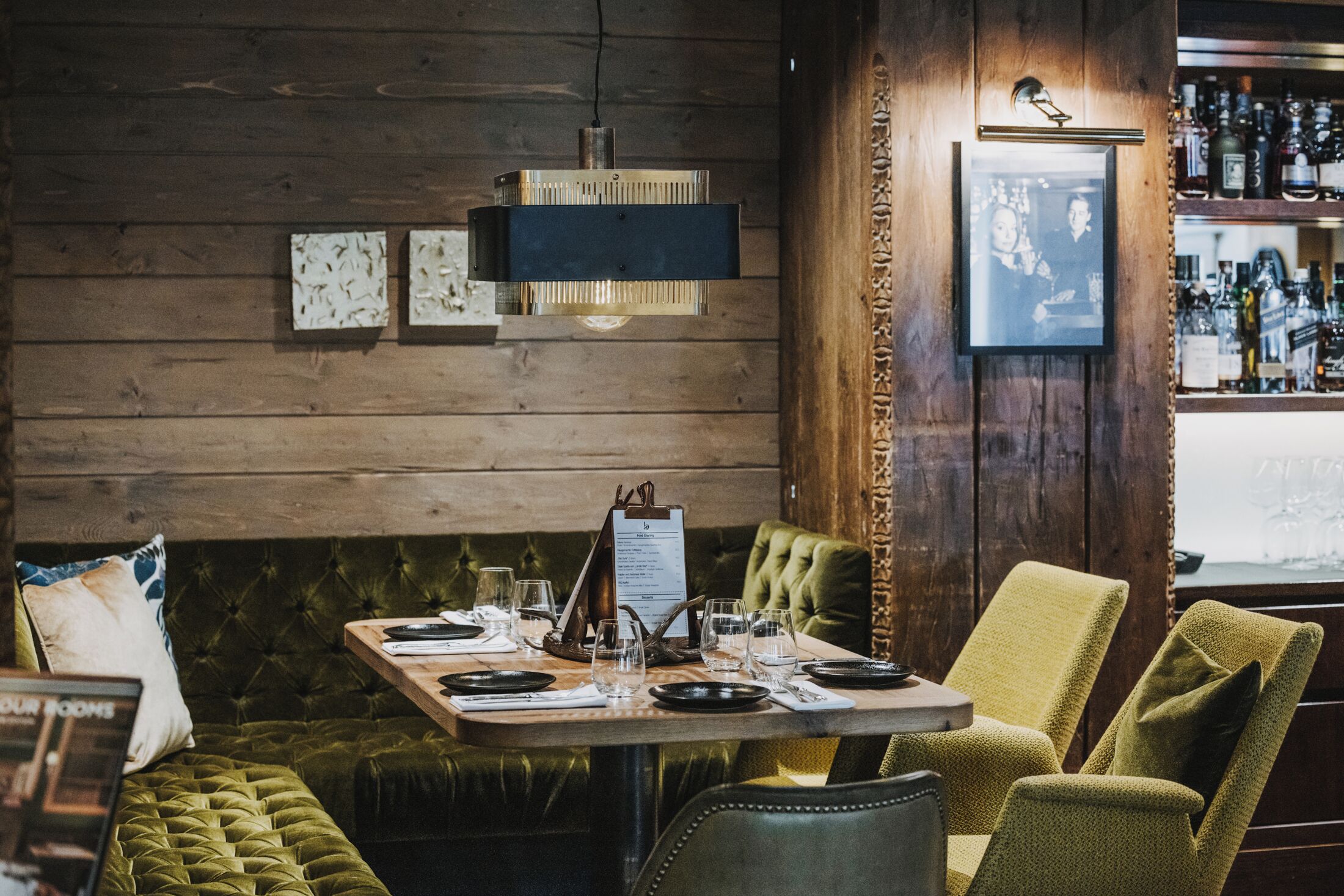 Un restaurante con pared de madera, un banco acolchado verde y una mesa preparada para comer.