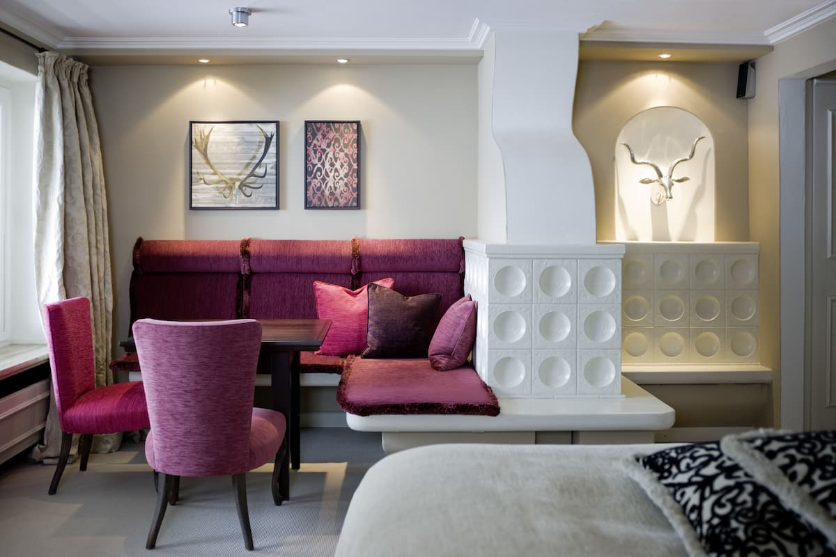 Une chambre d’hôtel moderne avec un canapé rouge, un fauteuil blanc et une cheminée décorative.