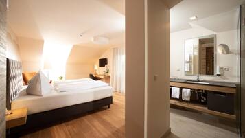 A modern bedroom with a large bed, a desk, and a bathroom with a mirror and sink.