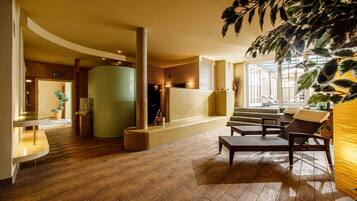 A spacious lobby with a wooden floor, a large green cylindrical structure, and a seating area with wicker chairs.