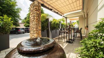 An outdoor patio area with a stone pillar, a water feature, and outdoor seating.