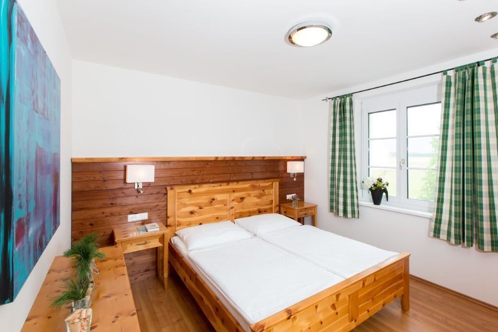 A wooden bed with white bedding, a nightstand, a wall-mounted lamp, and a window with green curtains.