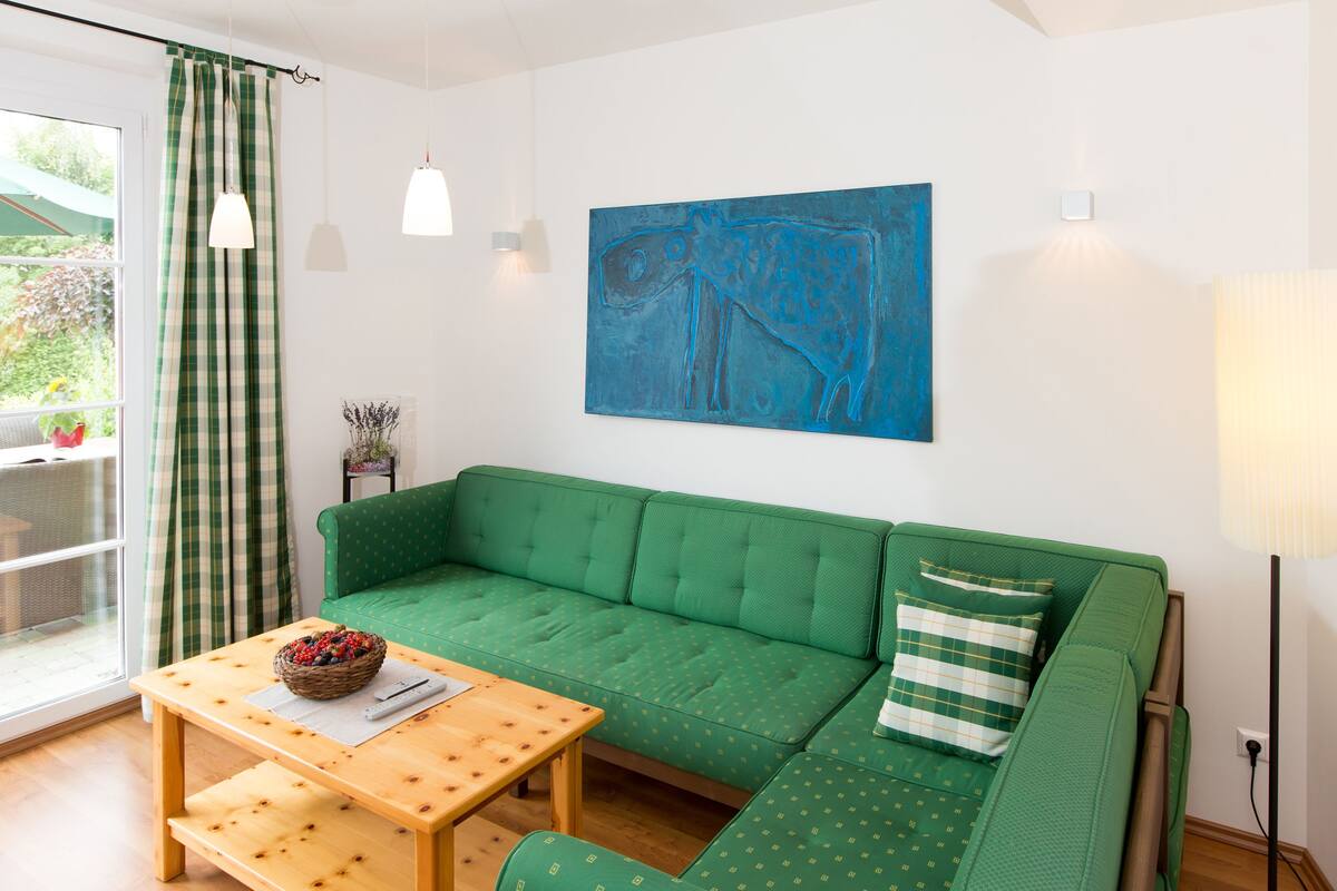 Un canapé vert, une table en bois avec un panier, et un tableau abstrait bleu accroché au mur.