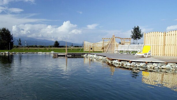 Ein ruhiger Poolbereich im Freien mit Holzterrasse, Liegestühlen und Holzumzäunung.