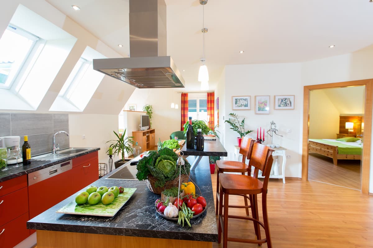 Une cuisine moderne dotée d’un îlot central, de meubles de rangement rouges et d’un coin repas avec des chaises en bois.