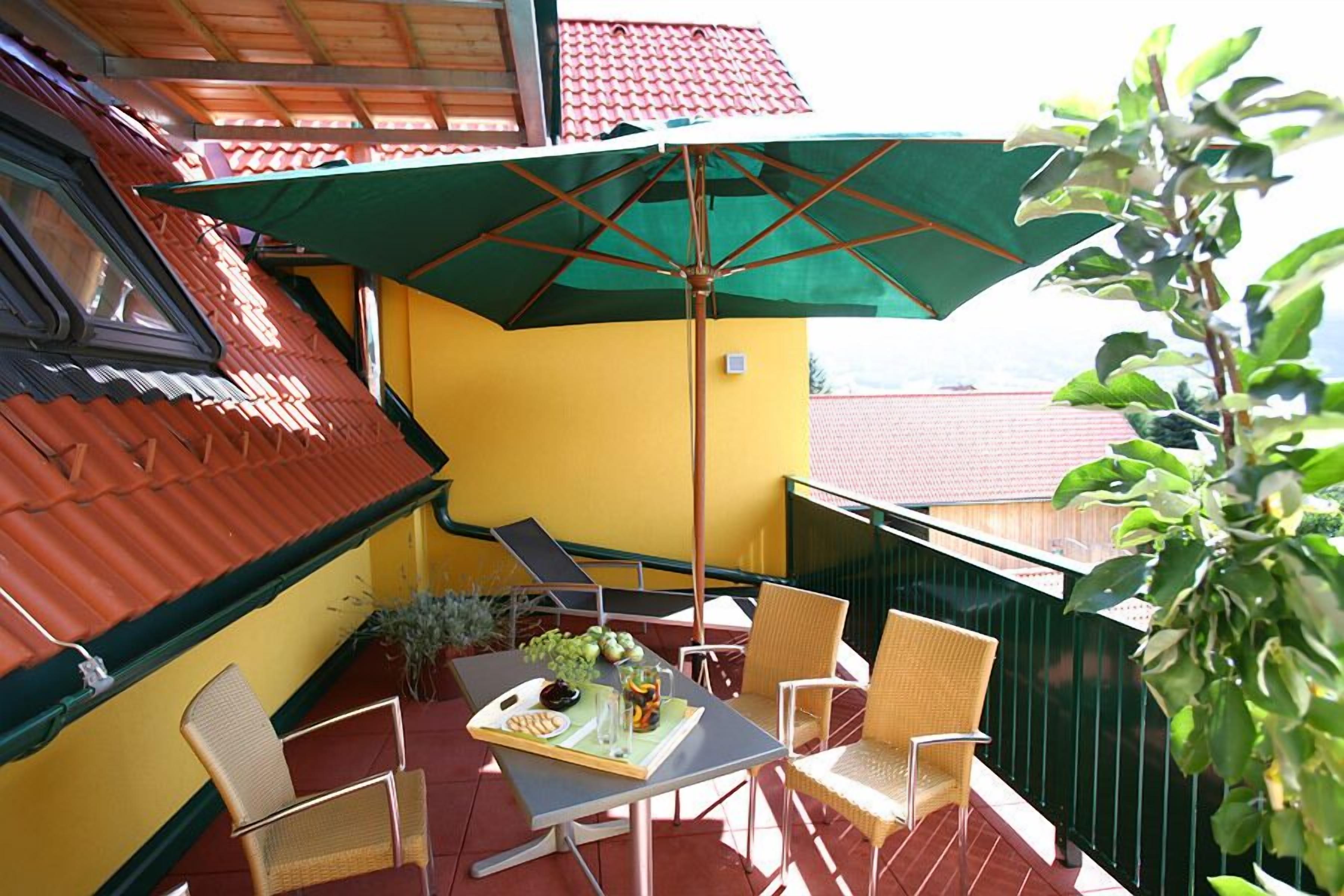 A balcony with a table, chairs, and a green umbrella.