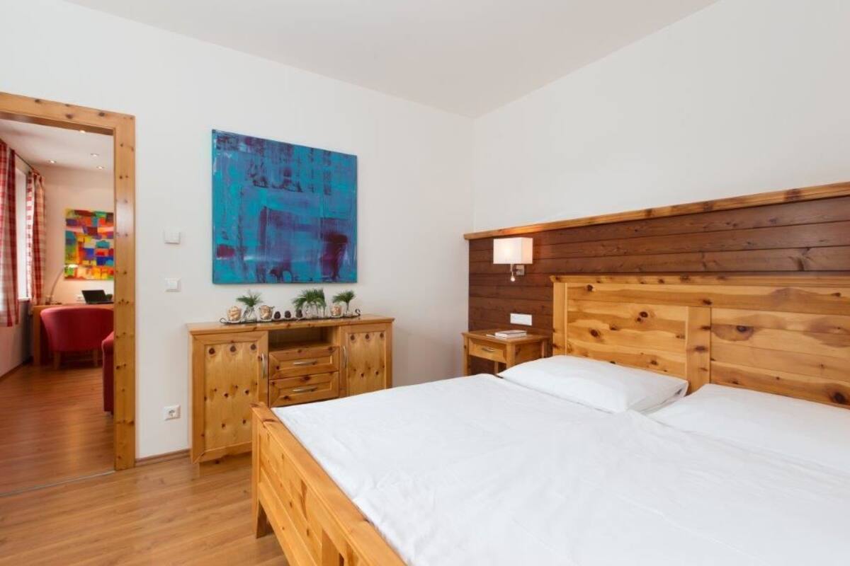 Une chambre à coucher avec un lit en bois, une table de chevet, une commode en bois et un tableau abstrait aux couleurs vives accroché au mur.