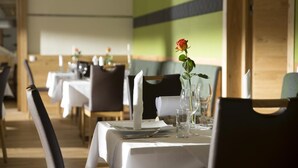 Interior de un restaurante con mesas dispuestas para comer, con manteles blancos, cristalería y un centro de mesa con una sola rosa.