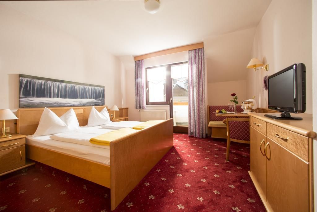 A hotel room with a bed, a desk, a television, and a window with curtains.