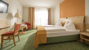 Habitación de hotel con cama, escritorio, silla, mesa y televisor.