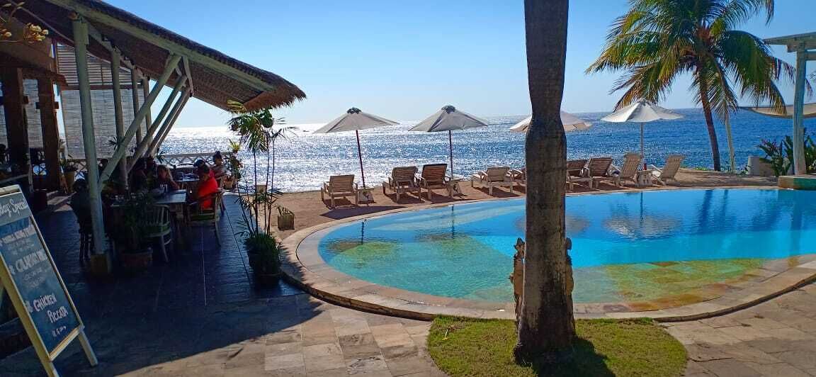 A poolside area with lounge chairs, a restaurant, and a view of the ocean.