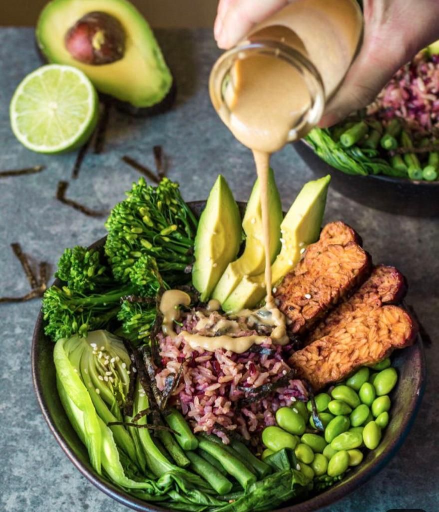 A bowl of food with various ingredients including rice, avocado, and green vegetables.
