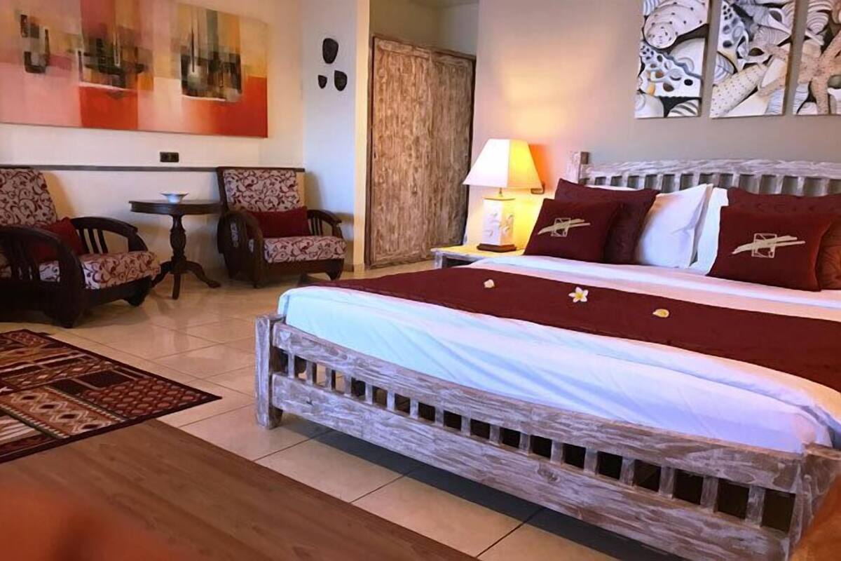 Een slaapkamer met een groot bed, twee stoelen, een kleine tafel en een lamp.