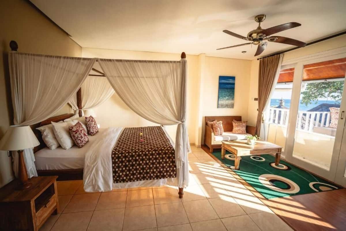 Een slaapkamer met een hemelbed, een plafondventilator, een bank en uitzicht op het omliggende landschap.