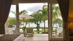 Une chambre d’hôtel avec un lit, une chaise en bois, une petite table et une vue sur une piscine et des palmiers.