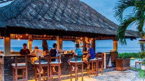 Un espace bar avec des chaises en bois et un toit de chaume, offrant une vue sur la mer.