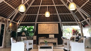 Un hall d’entrée spacieux avec un plafond haut et incliné, ainsi que de nombreux luminaires suspendus. On y trouve un comptoir de réception équipé d’un ordinateur et une grande œuvre d’art accrochée au mur.