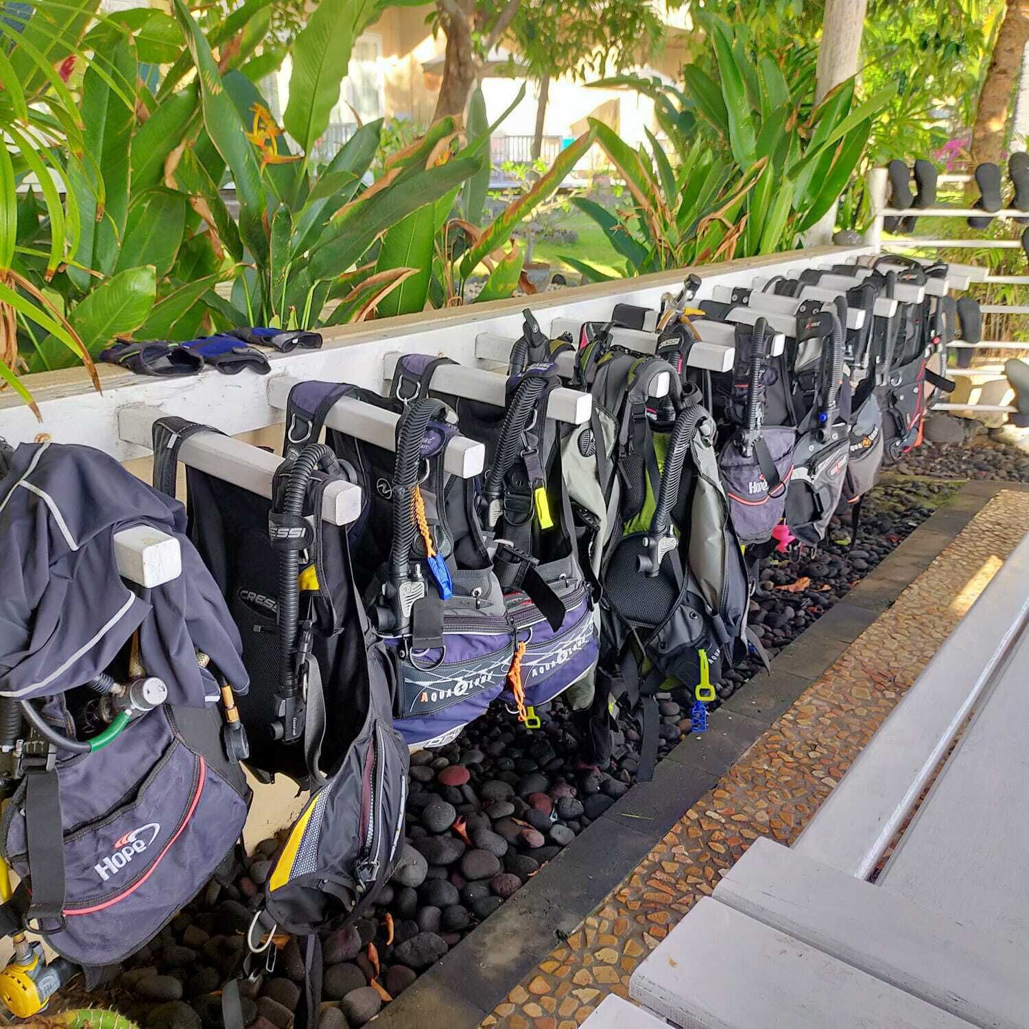 A row of bicycles with helmets and bags attached, parked on a stone pathway.