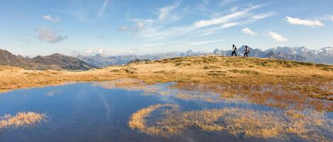 Ein weites Panorama einer Berglandschaft mit blauem Himmel und einem kleinen Gewässer, das die umliegende Landschaft spiegelt.