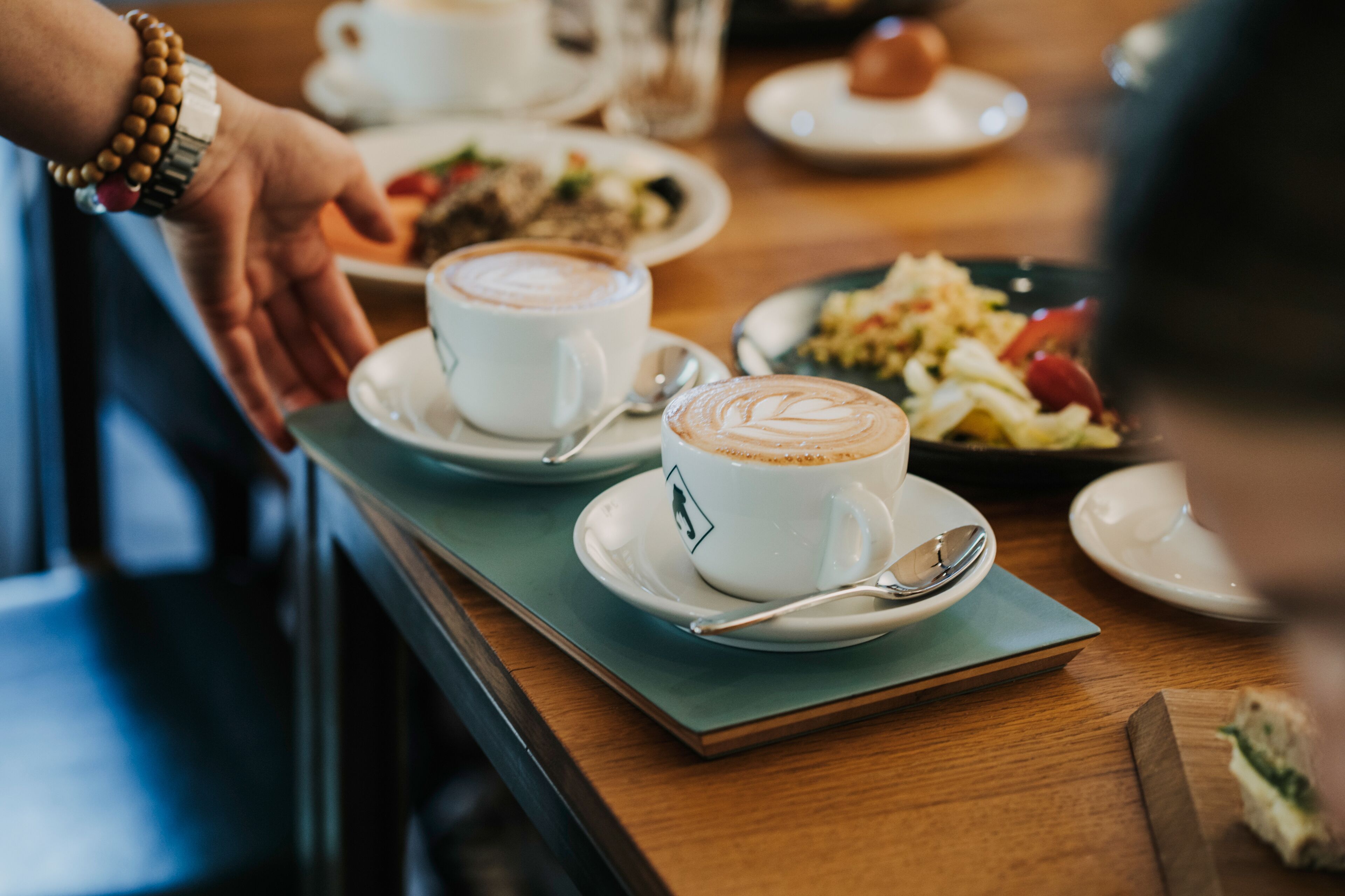 Una mesa con dos tazas de café, una cuchara y un plato de comida.