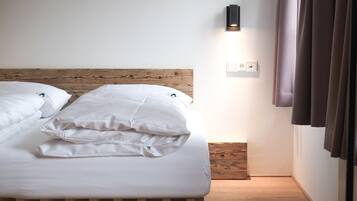 Una cama bien tendida con sábanas blancas, un cabecero de madera, un aplique en la pared y un enchufe.