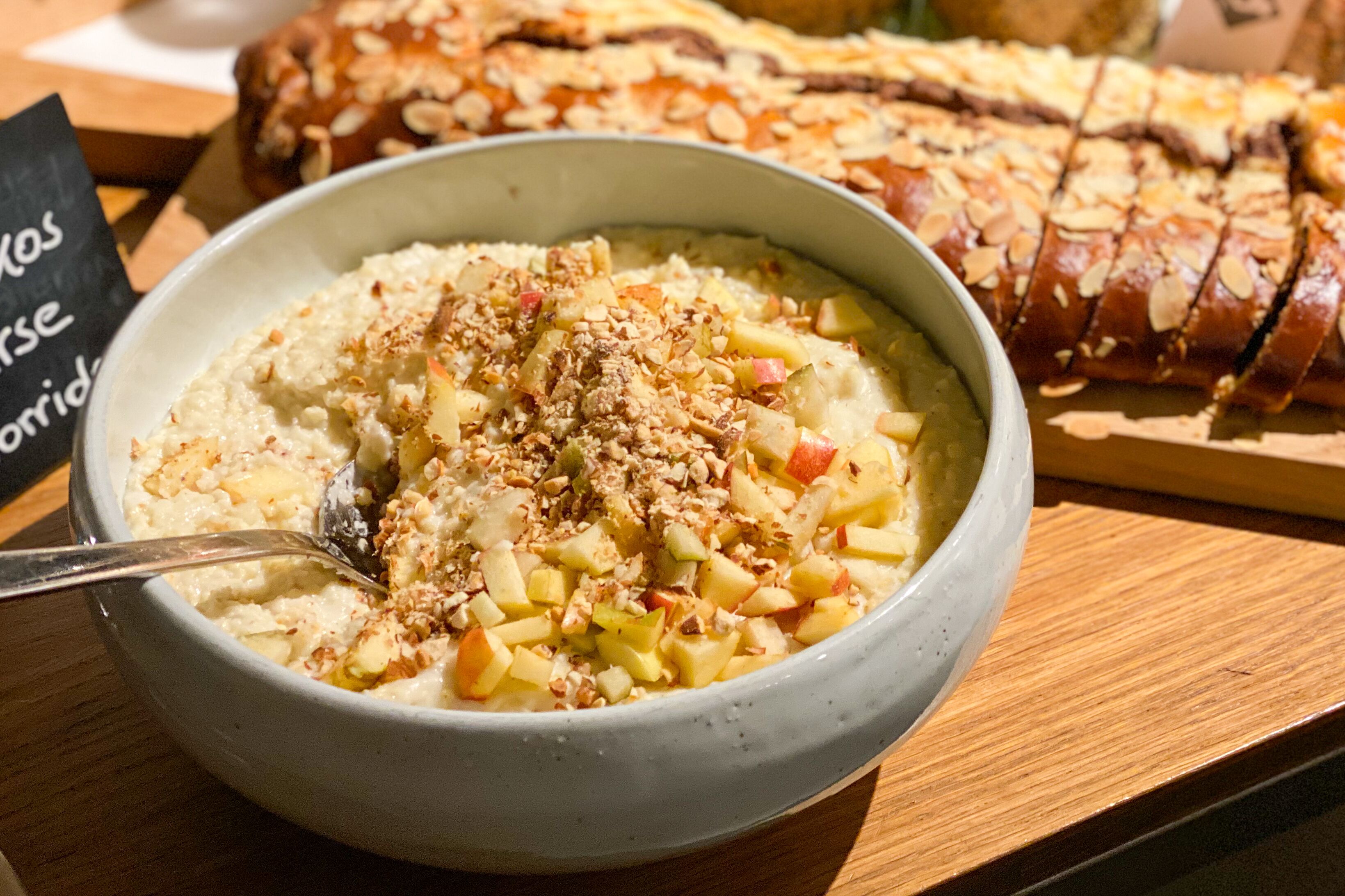Un tazón de avena cubierto de frutas y nueces, una hogaza de pan y un cartel con texto.