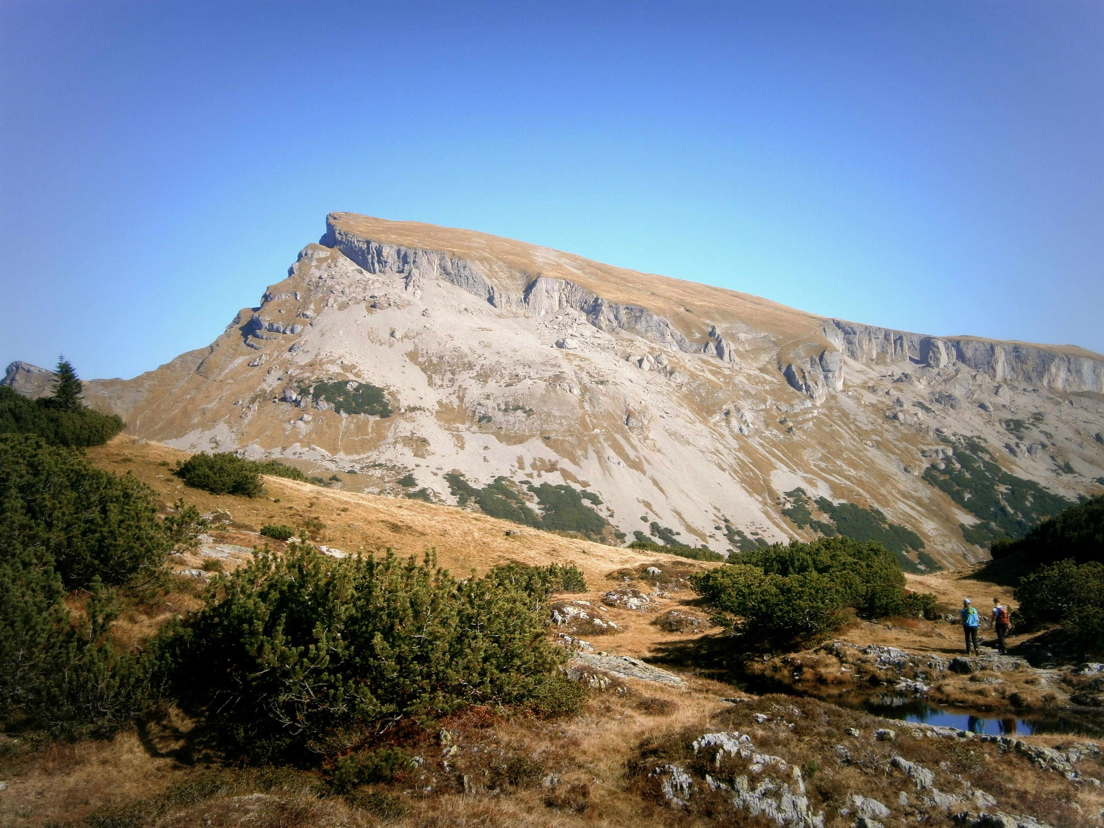 A mountainous landscape with a prominent rocky peak, a small stream, and sparse vegetation.