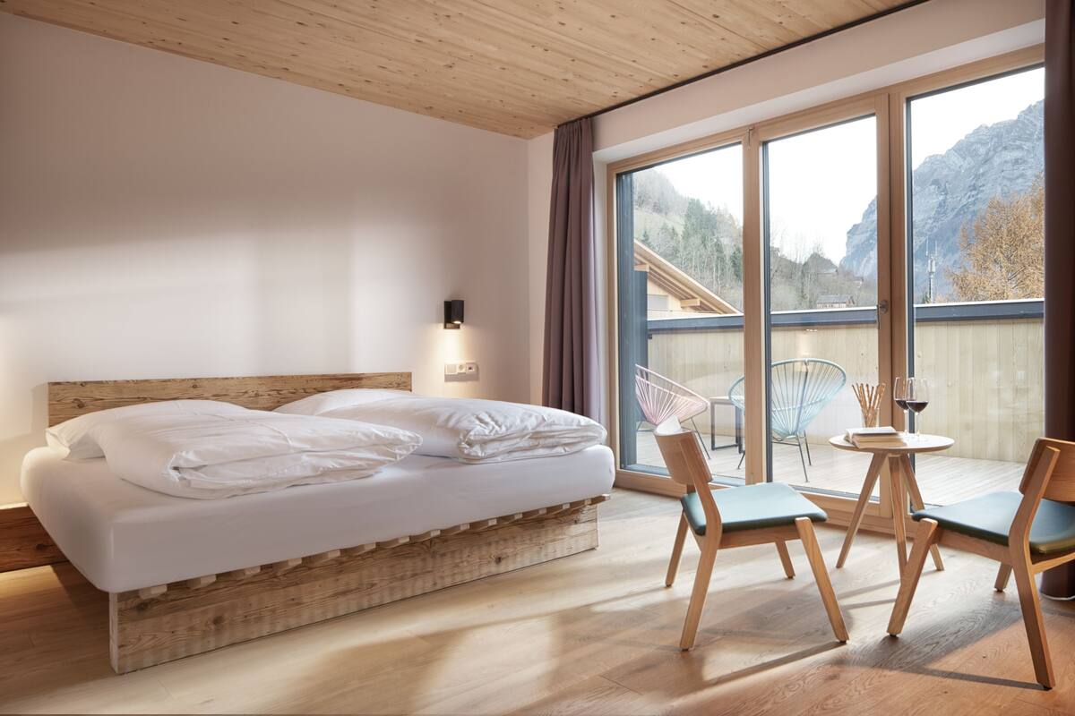 Une chambre à coucher avec un lit en bois, une petite table avec des chaises et une grande fenêtre donnant sur la montagne.
